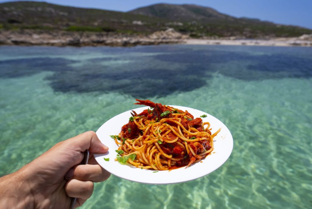 Un piatto di spaghetti con il sugo del pescato tenuto in mano sopra l'acqua turchese